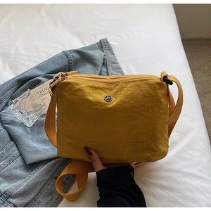 Detail of ginger yellow nylon crossbody bag with metal logo on soft white fabric