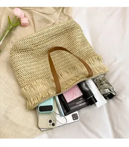 Detailed view of spacious straw tote bag with brown leather handles and fringe tassel decor