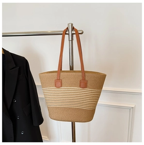 Detail of straw woven tote with beige stripes and brown leather shoulder straps