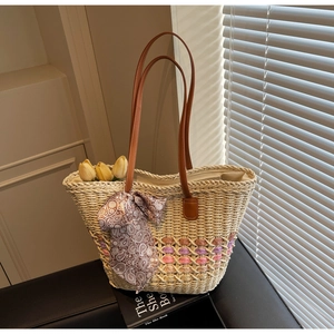 Close-up of woven straw tote bag with brown leather handles and decorative silk scarf