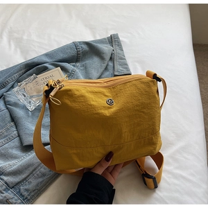 Detail of a ginger yellow nylon crossbody bag with dual zippers and adjustable strap