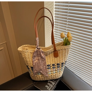 Detail of woven straw tote bag featuring brown leather straps and paisley silk scarf accessory