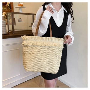 Detail of bohemian straw tote bag featuring decorative fringe and brown leather handles