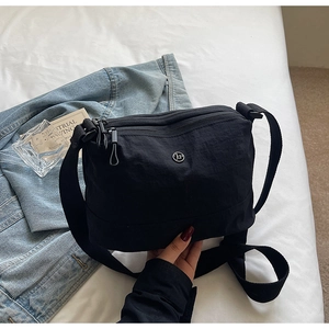 Close-up of black nylon crossbody bag with dual zippers and JP logo on a denim background