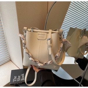 Close-up of beige bucket bag with lychee grain leather, logo detail and scarf-wrapped chain