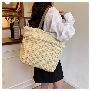 Close-up of woven straw tote bag featuring detailed fringe trim and brown leather straps