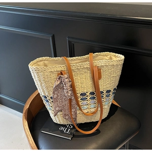 Detailed close-up of handmade straw tote bag with blue woven pattern and silk scarf handle