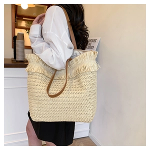 Straw woven tote bag with fringe details and brown PU straps shown in a lifestyle cafe setting