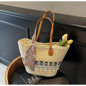 Detail of straw tote bag with blue contrast weave and brown leather handles with scarf
