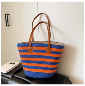 Detail of blue and orange striped straw tote bag with brown leather handles on a leather chair