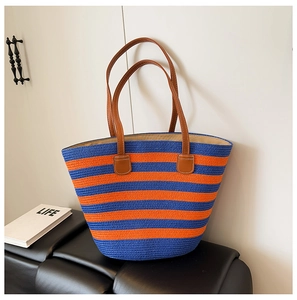 Detail of blue and orange striped straw tote bag with leather handles on black leather bench