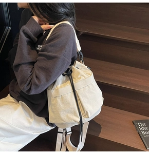 Detail van een crème bucket bag met dubbele zakken en een zwarte trekkoordsluiting
