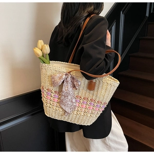 Detail of straw woven tote bag featuring floral ribbon bow and leather shoulder straps