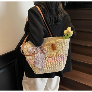 Detail of woven straw tote bag with multi-color base and paisley scarf on a leather handle