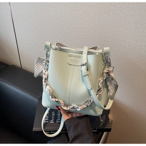 Close-up of light green lychee texture bucket bag with silk scarf wrapped chain strap