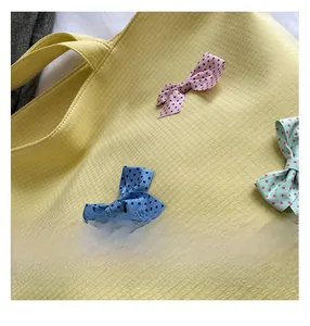 Close-up of polka dot bow charms in pink, blue and green on yellow waffle tote bag