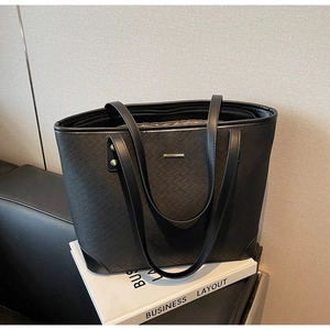 Close-up of black woven leather tote bag featuring a minimalist metal bar detail on front