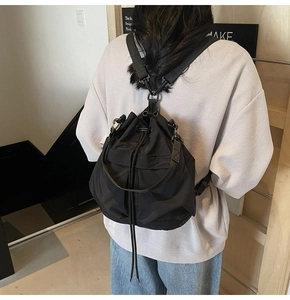 Detail van de zwarte nylon rugzak met trekkoord en metalen haken gedragen door een model