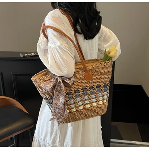 Detail of woven straw tote bag with brown leather straps and paisley silk scarf accessory