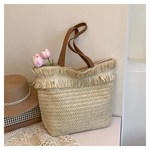Detail of a large straw tote bag with woven tassels and brown leather shoulder straps