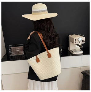 Detalle del bolso tote tejido beige con correas de cuero y sombrero de paja a juego