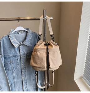 Detail van beige emmertas met trekkoordsluiting en afneembare riem aan een hanger