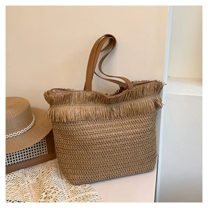 Close-up of woven straw tote bag featuring decorative fringe and brown leather straps