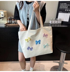 Close-up of beige canvas tote bag featuring colorful bow details and durable shoulder strap