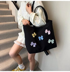 Detail view of a black canvas tote bag featuring colorful polka dot bows on a model