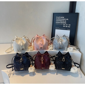 Close-up of textured bucket bags in various colors featuring plush doll charms and drawstrings