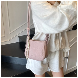 Pink lychee texture saddle bag featuring a unique knotted strap and woven pendant detail