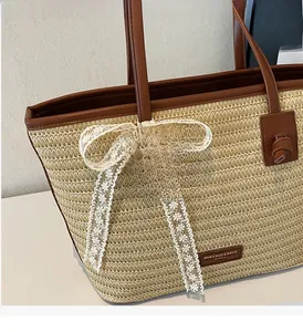 Détail du grand sac cabas en paille beige avec finitions cuir brun et nœud en dentelle