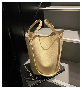 Close-up of beige lychee grain leather bucket bag on book with premium metal studs