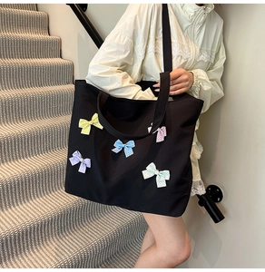 Close-up of black canvas tote bag featuring colorful polka dot bows on a checkered fabric