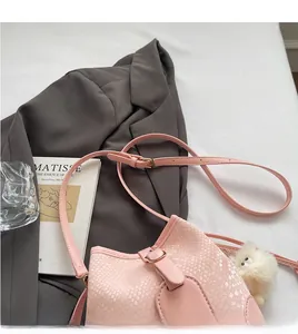 Detailed view of pink snake-pattern bucket bag with plush charm and adjustable strap