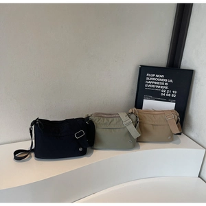 Three nylon crossbody bags in black, olive green, and khaki on a modern white display