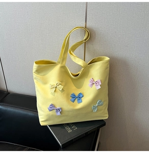 Detail of yellow canvas tote bag featuring colorful polka dot bows on textured fabric