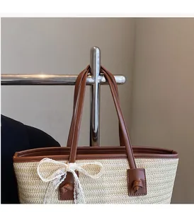 Détail du sac cabas en paille tissée avec poignée en cuir marron et grand nœud en dentelle