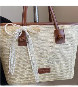 Détail d'un grand sac cabas en paille avec nœud en dentelle et plaque logo en cuir