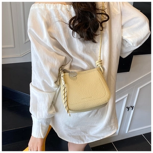 Close-up of yellow pebble leather bucket bag with tennis racket charm worn by a model