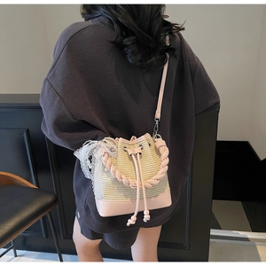 Detail of woven straw bucket bag with pink leather trim, lace accents, and pearl charms