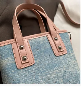Close-up of denim shoulder bag featuring pink leather handles and silver metal rivets