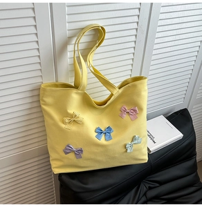 Detail of yellow canvas tote bag with five colorful polka dot bows on black cushion