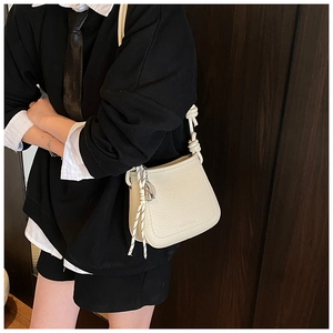 Detail of creamy white bucket bag featuring litchi leather texture and knot strap