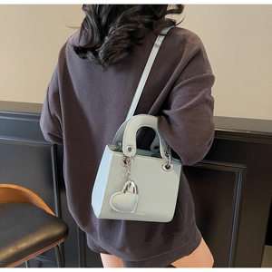 Detail of light blue crossbody bag with heart charm worn by model in a minimalist setting