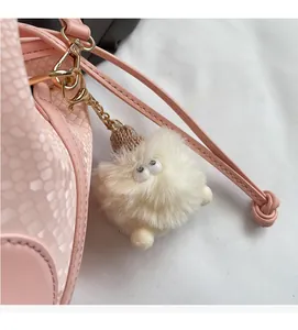 Detail of pink snakeskin texture handbag featuring a cute beige furry monster charm