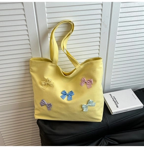 Detail of yellow canvas tote bag featuring multi-colored bow decorations on black surface