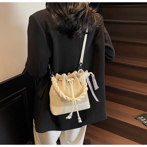 Detail of woven straw bucket bag with lace bow, pearl charm and drawstring closure