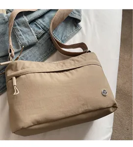 Close-up of khaki nylon shoulder bag fabric and logo detail on a white bed sheet