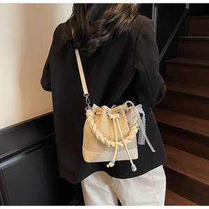 Detail of a beige woven bucket bag featuring elegant lace ribbons and pearl pendants